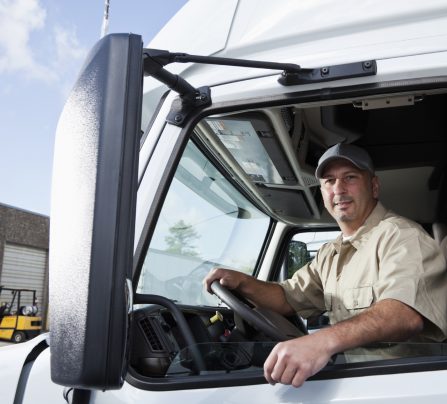 Truck driver (30s) sitting in cab of semi-truck.